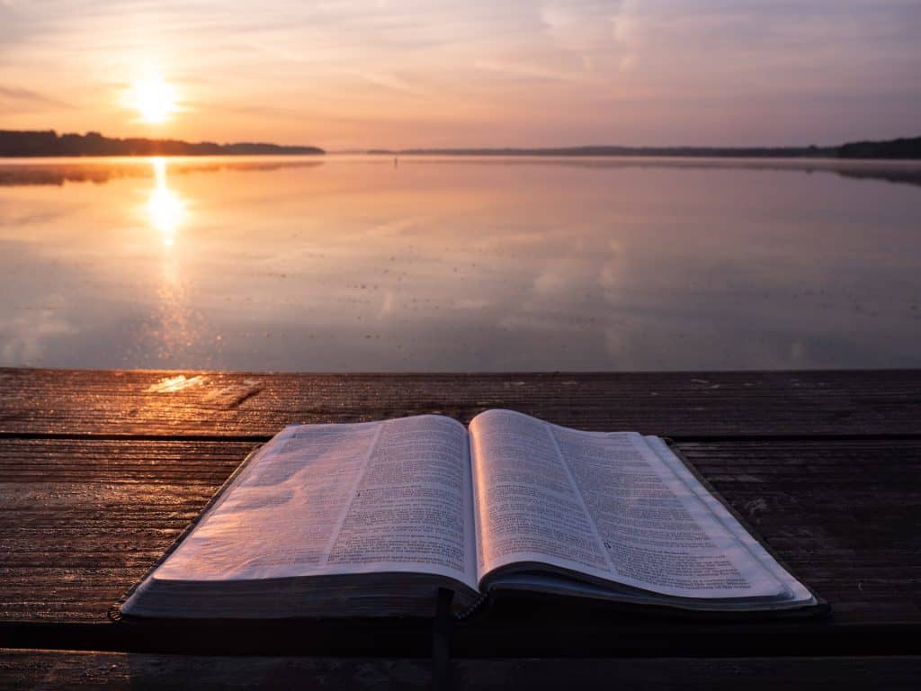 A Bible in the front of a lake and sun is shining on the Bible